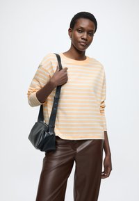 Cămașă cu mâneci lungi cu dungi în galben deschis și gri, cu decolteu rotund. Asortată cu pantaloni maro din piele ecologică și o geantă mică neagră.