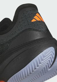 Scarpa sportiva nera con tomaia testurizzata, dotata di un logo arancione e suola ammortizzata. Particolari modelli scanalati sulla suola esterna.