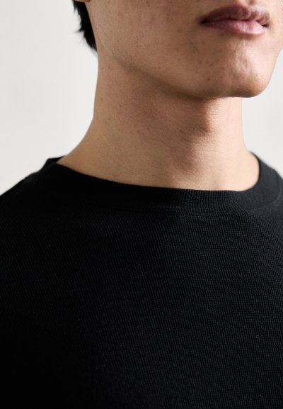 Schwarzer gerippter Rundhals-Pullover, der den Hals- und oberen Brustbereich zeigt, mit einer glatten Textur und nahtlosem Design.
