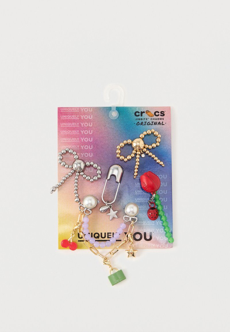 Set van Jibbitz charms met gouden en zilveren kralen, een veiligheidsnaald, een roos, groene en paarse kralen, en een lieveheersbeestje. Kleurrijke achterkaart.