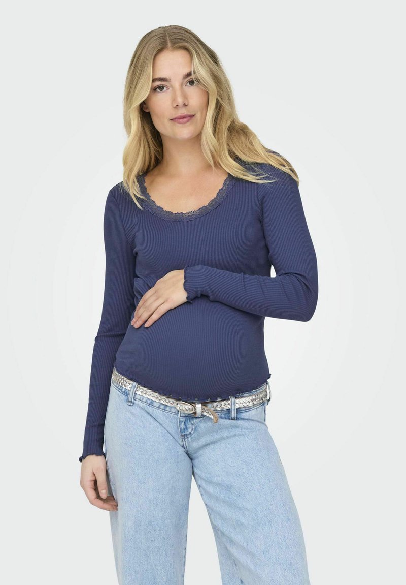 Langarm-Oberteil in Marineblau mit Rippstruktur und Spitze am Halsausschnitt sowie an den Ärmeln, kombiniert mit hellblauen High-Waist-Jeans und einem geflochtenen silbernen Gürtel.