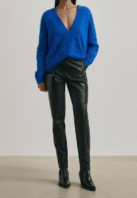 Niebieski dziergany sweter z dekoltem w serek i ażurowym wzorem, zestawiony z czarnymi skórzanymi spodniami oraz botkami na kostkę.