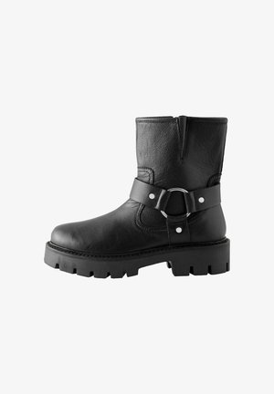 Zwarte leren enkellaars met een gestructureerd oppervlak, ronde neus, chunky rubberen zool en een zijriem met een zilveren gesp en studs.