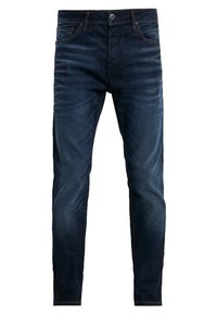 Jean en denim bleu foncé avec une coupe slim, présentant des coutures contrastées et une fermeture éclair. Texture lisse avec un léger délavage sur les cuisses.