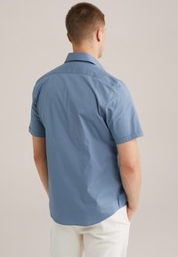 Camisa de manga corta, de color azul, con un cuello tipo polo, fabricada en tela suave. Presenta un dobladillo curvado y un diseño mínimo en la parte posterior.