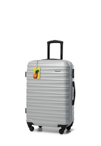Silver hard-shell suitcase with a ribbed texture, two wheels, a telescopic handle, and a yellow pineapple-shaped luggage tag attached.