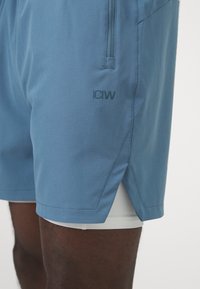 Shorts de sport bleus fabriqués en matériau léger, dotés d'un logo, de poches latérales et d'une doublure intérieure blanche contrastante.