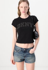 Mustat lyhythihaiset t-paidat, joissa on strassikoristeet, jotka spellittävät "DKNY NEW YORK", yhdistettynä sinisiin farkkushortseihin ja pieneen mustaan olkalaukkuun.
