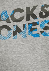 T-shirt grigio in cotone con grande testo stampato in nero e blu con un motivo testurizzato. Il testo recita "BACKS & BONES."