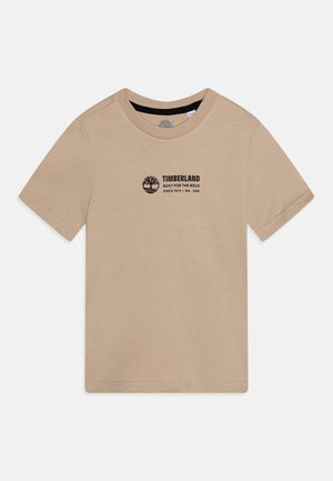 Camiseta beige de manga corta Timberland con cuello redondo y texto de logo negro "Built for the Bold Since 1973 / NH USA" en el pecho.