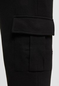 Pantaloni cargo negri cu un buzunar lateral cu clapetă, fabricați dintr-un material moale din bumbac cu o textură netedă și o croială adaptată.
