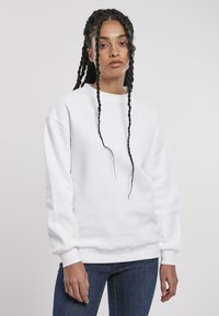 Felpa bianca con maniche lunghe, scollatura rotonda e polsini a coste. Indossata con jeans blu, esposta su uno sfondo neutro.