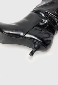 Stivali ankle in pelle nera con finitura lucida, dotati di punta affusolata e tacco piccolo e snello. Superficie testurizzata con motivo coccodrillo.