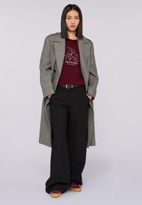 Cappotto di lana grigio su una camicia bordeaux con grafica. Pantaloni larghi neri con tasche. Scarpe bordeaux e beige. Design semplice, senza motivi.