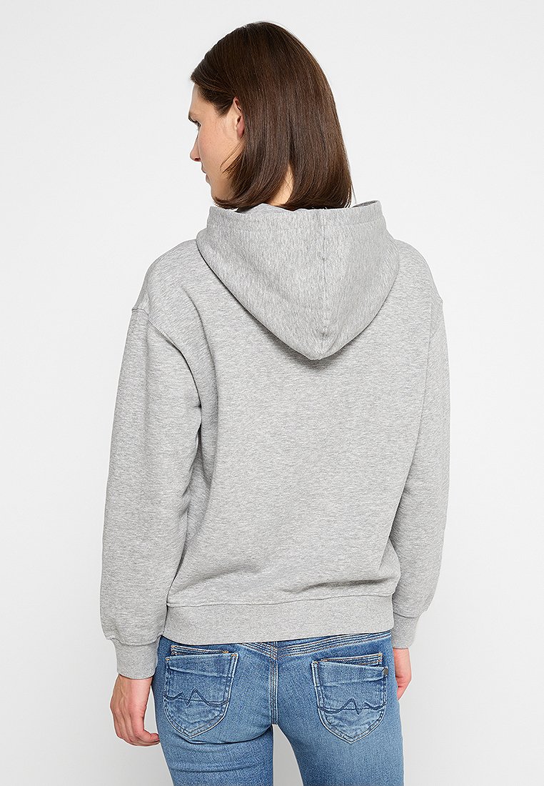 Felpa grigia con cappuccio regolabile, polsini e orlo a coste, abbinata a jeans blu, che mostra una texture in pile spazzolato. Design semplice, senza fantasie.
