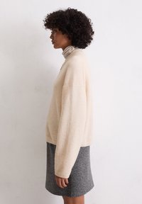 Maglione beige testurizzato con spalle scese abbinato a una gonna corta grigio antracite. La vista laterale mette in evidenza il fit rilassato e i dettagli del tessuto.