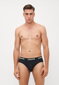 Bóxers negros de Levi's con una cinturilla elástica que presenta texto de logo en blanco. Tejido suave con un diseño ajustado, modelo de pie frente a un fondo liso.
