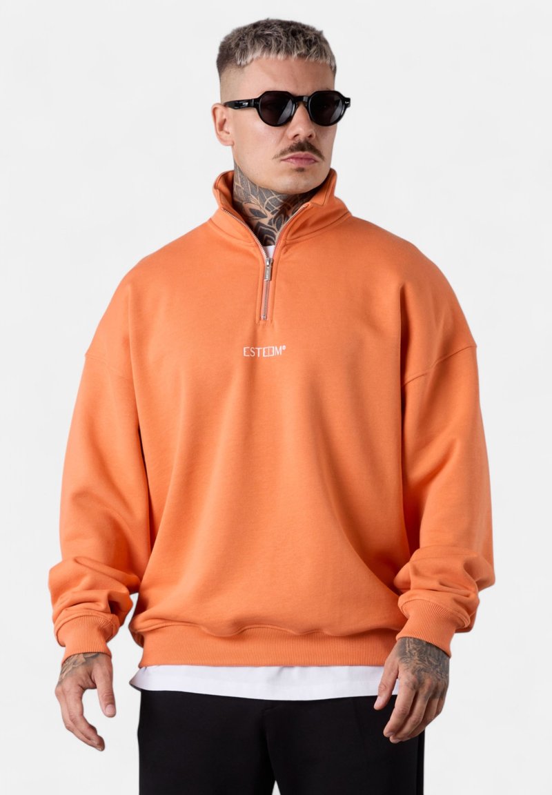 Oranges Fleece-Sweatshirt mit hohem Kragen und halbem Reißverschluss. Mit gerippten Bündchen und Saum, sowie weißem "ESTEEM"-Branding auf der Brust.