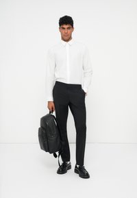 Weißes Button-up-Hemd, schwarze maßgeschneiderte Hose, schwarzer Leder-Rucksack und schwarze Schuhe mit dicken Sohlen. Einfaches, sauberes Design mit minimalen Akzenten.