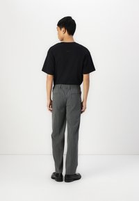 Black short-sleeve t-shirt paired with gray pinstripe trousers, elastic waistband, and black shoes, viewed from the back.