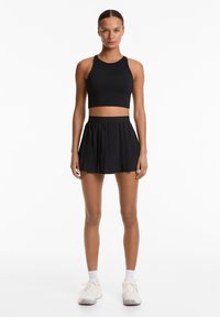 Black athletic crop top with a round neck and fitted design, paired with a pleated black skirt. Footwear includes white sneakers and ankle socks.
