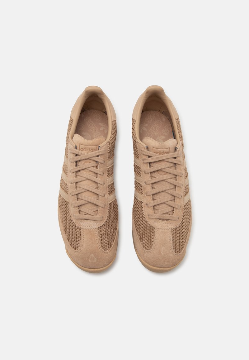 Zapatillas deportivas beige con materiales de malla y ante, que presentan rayas tonales, puntera redondeada y acentos texturizados en los laterales.