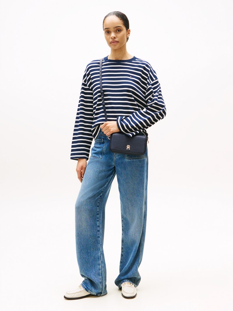 Maglia a righe navy e bianca a maniche lunghe, jeans blu larghi e scarpe bianche. Borsa a tracolla navy con un sottile dettaglio del logo.
