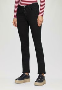Czarne dżinsy o slim fit z pięcioma guzikami i gładką teksturą. Sparowane z czarnymi sneakersami na platformie z beżową podeszwą.
