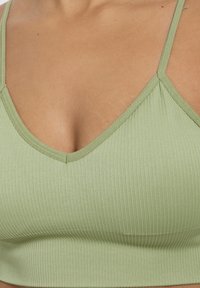 Bralette de color verde claro con diseño de cuello en V y tirantes finos ajustables. Textura suave con detalles de costura a lo largo del escote.