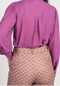 Blusa viola con texture e maniche a sbuffo abbinata a pantaloni beige a vita alta con un motivo floreale rosa e tasche posteriori.