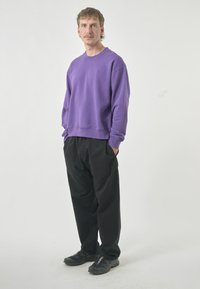 Purple crew-neck sweatshirt, loose fit, with ribbed cuffs and hem. Black, loose-fitting pants. Dark athletic shoes with multi-colored accents.