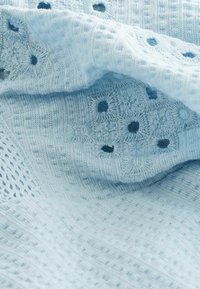 Tissu tricoté bleu clair avec un motif texturé de petits dessins circulaires bleu foncé en forme de fleurs et des carrés à tissage ouvert.