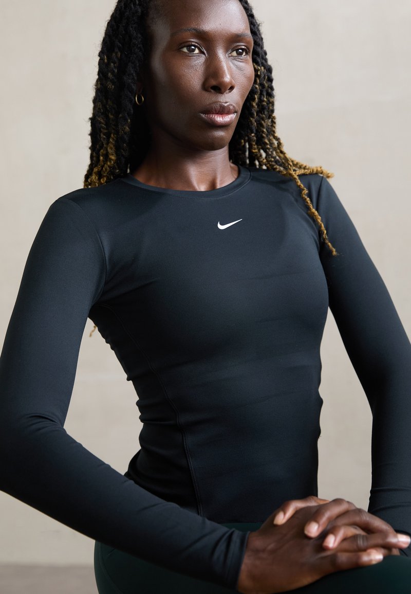 Svart langermet treningsgenser med rund hals og Nike-logo. Glatt tekstur og tettsittende design som fremhever kroppens form.