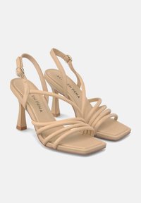 Sandalias de tacón alto beige con diseño de punta cuadrada, tiras texturizadas y un tacón geométrico delgado. Cierre de hebilla en el tobillo.