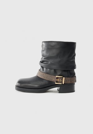 Bota ankle em couro preto com um design solto, apresentando um cinto decorativo castanho com uma fivela dourada e um salto baixo e grosso.