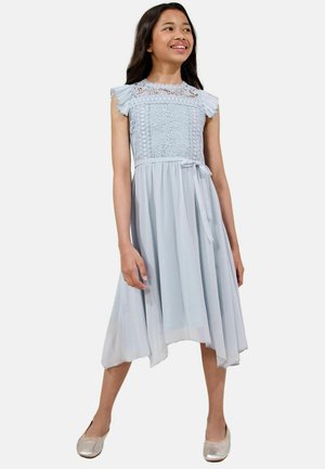 Hellblaues Kleid mit Spitzen-Bustier und schwingenden Ärmeln, tailliert, mit fließendem Rock und asymmetrischem Saum, kombiniert mit silbernen Schuhen.