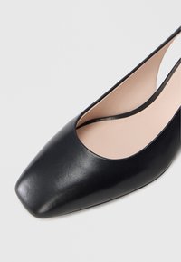 Juodi odiniai aukštakulniai batai su kvadratine nosimi ir žemu kirpimu. Lygus paviršius su kontrastuojančia kūno spalvos vidpadžio dalimi.