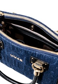 Sac à main texturé bleu marine avec quincaillerie dorée, fermeture éclair et anse en cuir noir. L'intérieur comporte plusieurs compartiments.