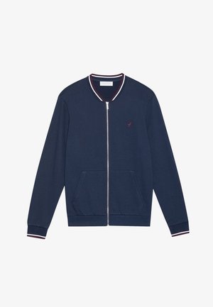 Tumši zils džemperis ar rāvējslēdzēju, izgatavots no mīksta auduma, ar ribotu apkakli sarkano un balto svītru kombinācijā, divām priekšējām kabatām un mazu logotipu uz krūtīm.