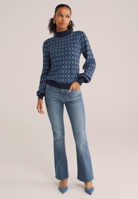 Pullover navy con motivo geometrico, maniche lunghe e orlo a costine, abbinato a jeans a zampa d'elefante azzurri e décolleté blu a punta.
