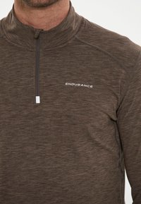 Brun zip-up pullover lavet af tekstureret stof med en høj krave, der har reflekterende hvide "ENDURANCE" branding på brystet.