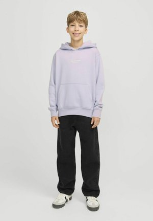 Sweatshirt à capuche violet clair avec une poche frontale, associé à un pantalon large noir et des baskets blanches avec des accents noirs.