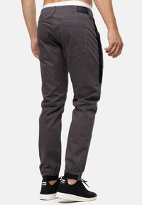 Los pantalones de chándal grises presentan una cinturilla elástica, un diseño ajustado y dos bolsillos traseros. Se combinan con unas zapatillas negras con textura.