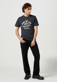 Camiseta gris oscuro con una impresión gráfica blanca que dice "Ride of Life Wrangler", combinada con pantalones negros y zapatos negros.