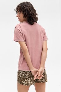 Pink short-sleeve t-shirt with a round neckline, worn with leopard print shorts. The fabric appears soft and slightly textured.