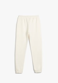 Cremefarvede sweatpants lavet af blødt stof. De har et elastisk liv og ribbede manchetter ved anklerne for en tætsiddende pasform.