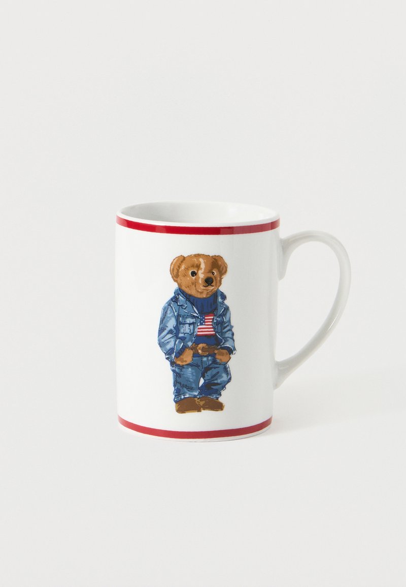 Cana albă din ceramică cu margini roșii, având imprimată o imagine cu un urs care poartă o jachetă din denim, blugi și un pulover cu steagul american.