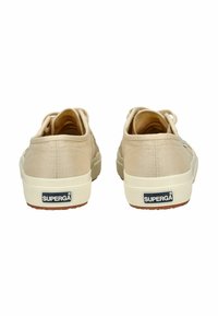 Zapatillas de lona beige con suela de goma texturizada, presentando un diseño de cordones y un logo negro de Superga en el talón.