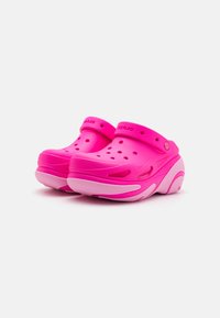 Rosa träskor med slip-on design, som har ventilationshål, ett stabilt spänne och en tvåfärgad sula med en texturerad yta.
