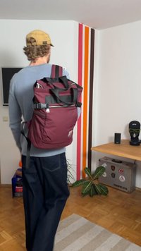 Mørkerød ryggsekk med to stropper, frontlomme med glidelås og en blank svart detalj. Laget av slitesterkt stoff, formet for ergonomisk bruk.